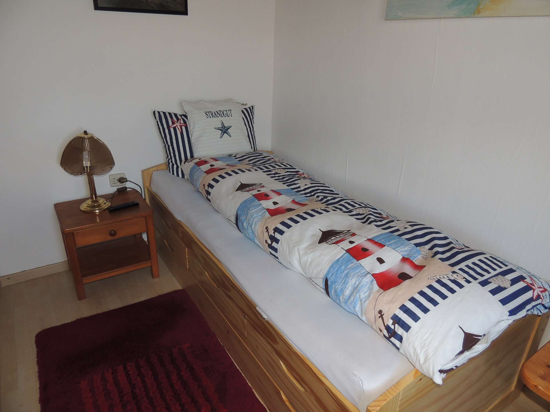 Einzelzimmer Bett mit Leuchtturmbettwäsche und Nachttisch